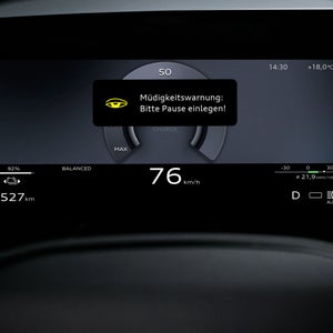 Nahaufnahme eines Displays im Fahrzeuginnenraum. Abgebildet ist sehr prominent eine Meldung "Müdigkeitswarnung: Bitte Pause einlegen!".