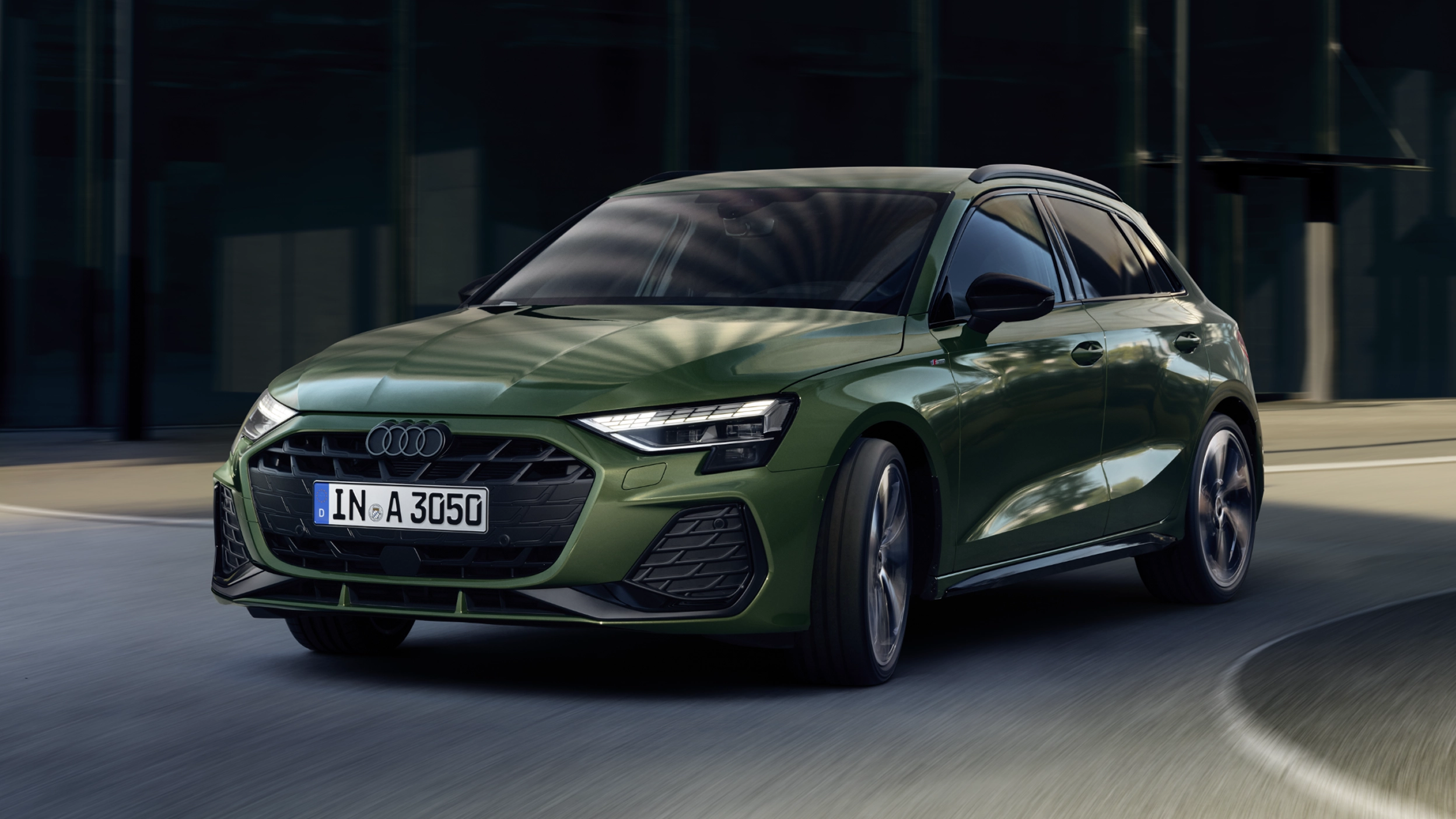 Landscape image of a green Audi A3 Sportback against in an urban setting.