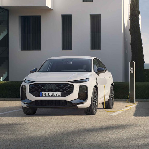 A white Q3 Sportback e-hybrid parked in front of a modern house is charging at a public charging station.