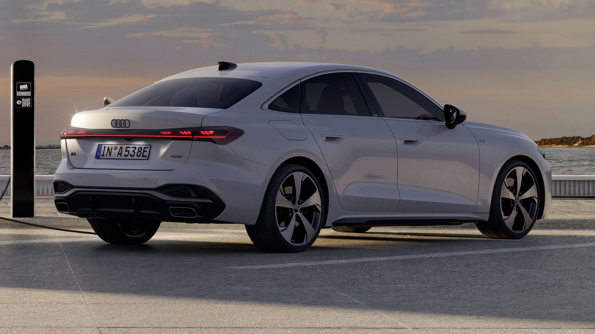 Die A5 Limousine e-hybrid steht im schrägen Heckprofil auf einem Parkplatz und ist an eine Ladestation angeschlossen.