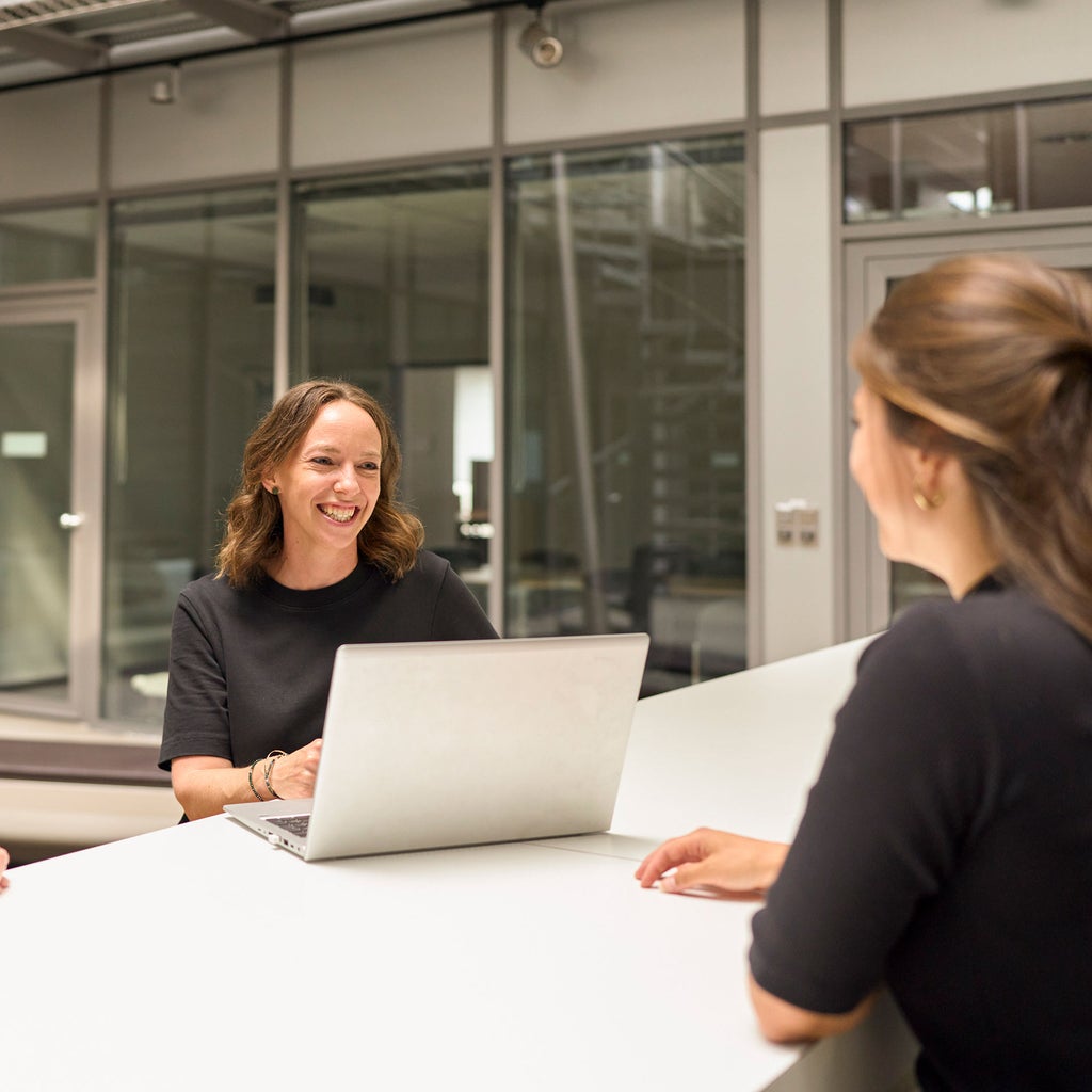 Melanie Limmer lacht eine Kollegin an und hat einen Laptop vor sich