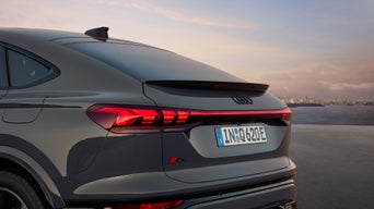 Rear view of a sleek Audi Q6 Sportback e-tron, showcasing elegant taillights, sporty spoiler, and urban skyline in the background at sunset.