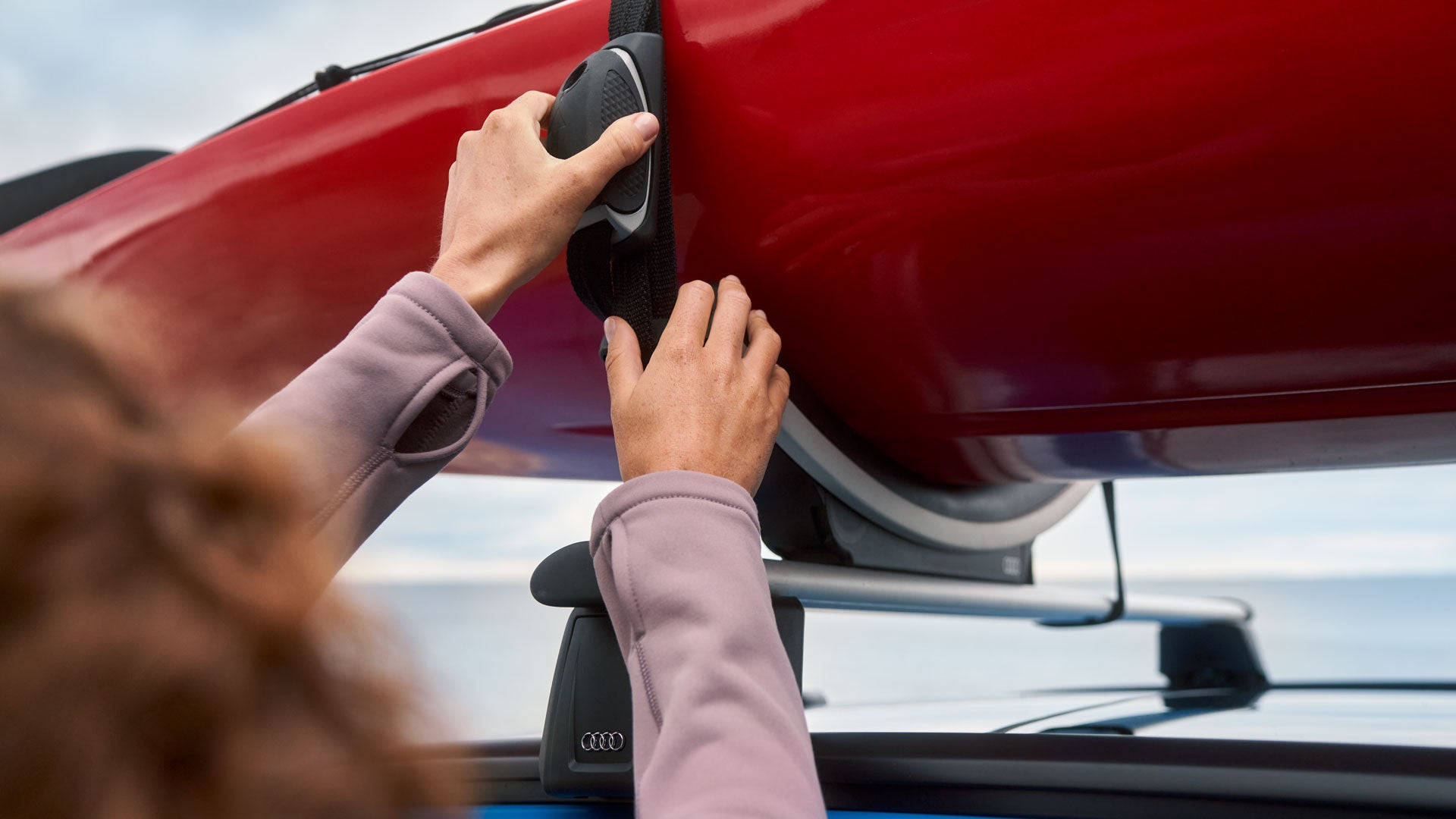 Person befestigt ein rotes Kajak mit einem Spanngurt auf dem Dachträger eines Autos