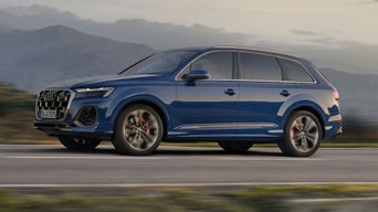 A blue Audi SUV in motion on a road with a mountainous backdrop.