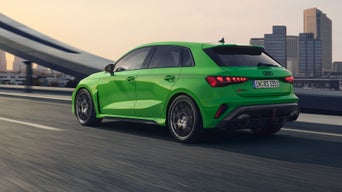 Grüner Audi RS 3 Sportback fährt auf einer Brücke vor städtischer Skyline.