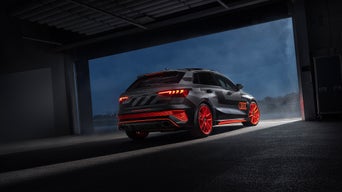 Audi RS 3 driving experience (rear view) is parked in an open garage, outside it is dark and hazy.