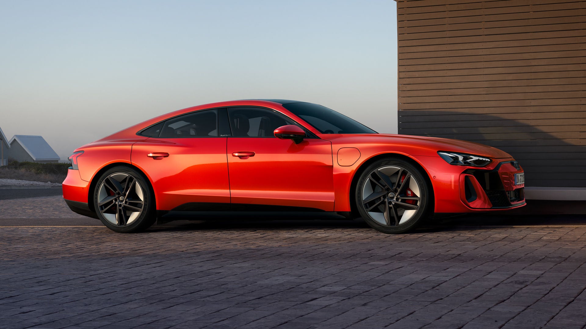 Ein roter Audi S e-tron GT parkt neben einem Haus, eine minimalistische Architektur und ruhige Landschaft im Hintergrund.