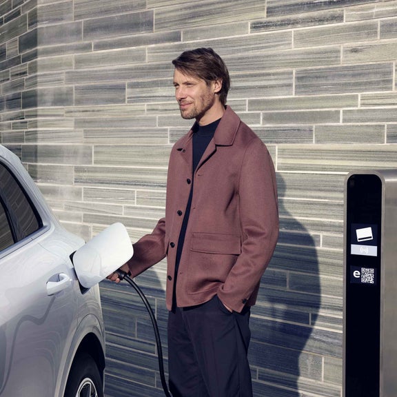A young, smiling man connects the Q5 SUV e-hybrid to a charging station.