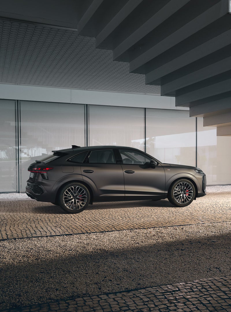 The Audi Q3 Sportback stands in a dim light under a staircase. The car can be seen from the side, showing the exact details of the exterior.