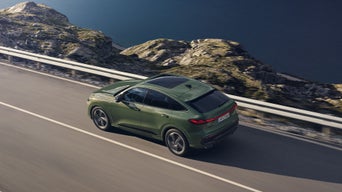 Un Audi Q5 Sportback vert olive roule sur une route sinueuse le long d'un paysage montagneux.