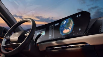 Eine lächelnde Frau steht unter einem Carport und bedient ein Tablet. Im Hintergrund steht ein silberfarbener Audi A6 e-tron.