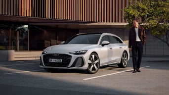 Frau in High Heels geht vor einem parkenden, blauen Audi Q8 SUV e-tron und modernem Gebäude entlang.