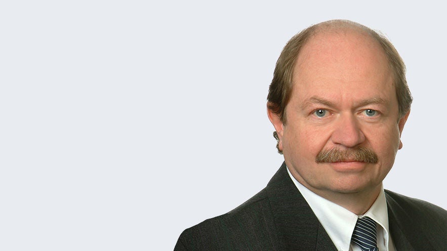 Josef Büchl: Porträt eines älteren Mann mit Oberlippenbart im Anzug mit gestreifter Krawatte vor hellgrauem Hintergrund.