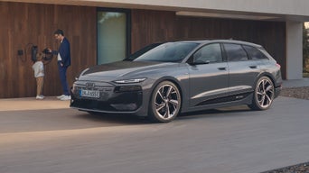 Grauer Audi A6 Avant e-tron parkt vor einem Haus, ein Mann und Kind stehen an der Ladestation.