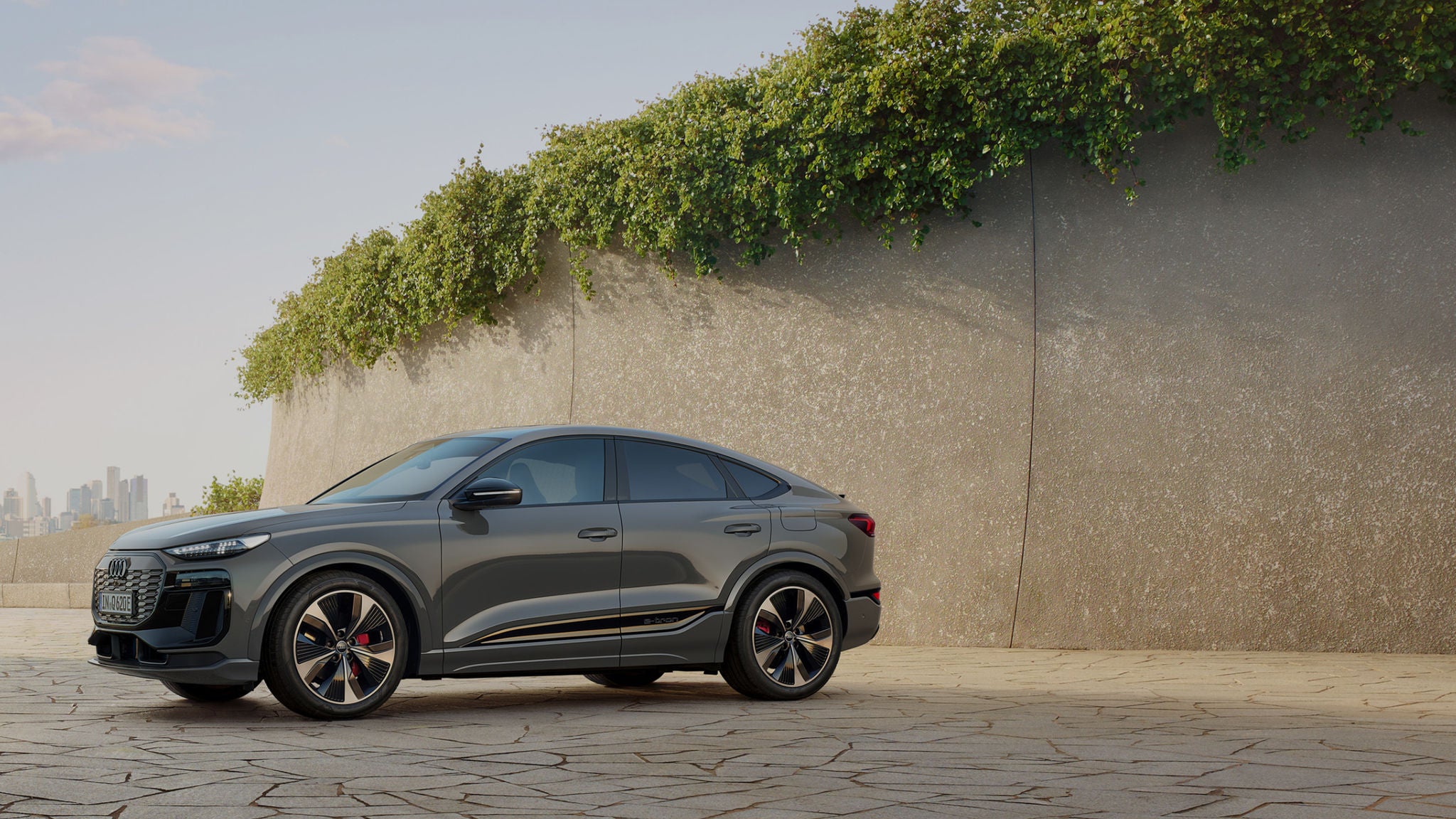Audi Q6 Sportback e tron parked on a modern designed cracked patio with plants and city skyline in the background.