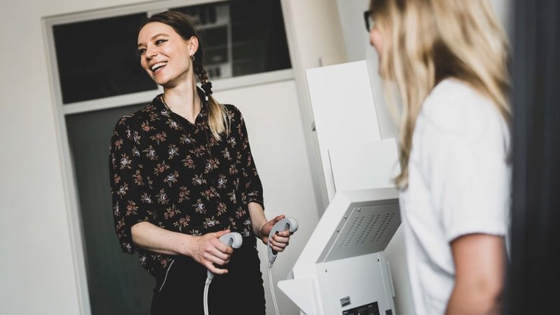 Two people are standing in a room and jointly operating a medical device.