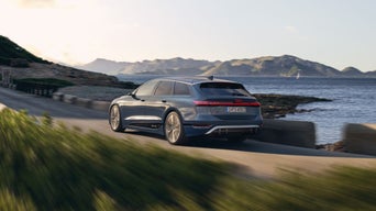A grey Audi e-tron driving along a coastal road with hills and sea in the background