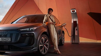 A person in a trench coat charging an electric SUV at a charging station.