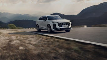 White Audi Q3 Sportback e-hybrid plugged into a modern charging station in an urban outdoor setting.