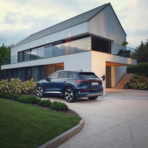 De Q4 e-tron laadt op via een wandkast op de oprit van een modern huis.