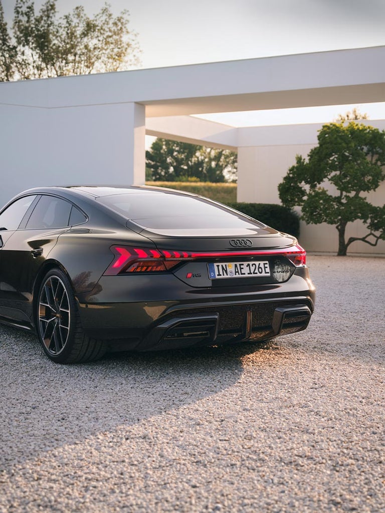 Schwarzer Audi RS e-tron GT auf Kiesplatz mit moderner Architektur und Garten im Hintergrund.