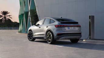 Silberner Audi Q4 Sportback e-tron mit Sportfelgen lädt an einer Ladesäule vor modernem Gebäude bei Sonnenuntergang.