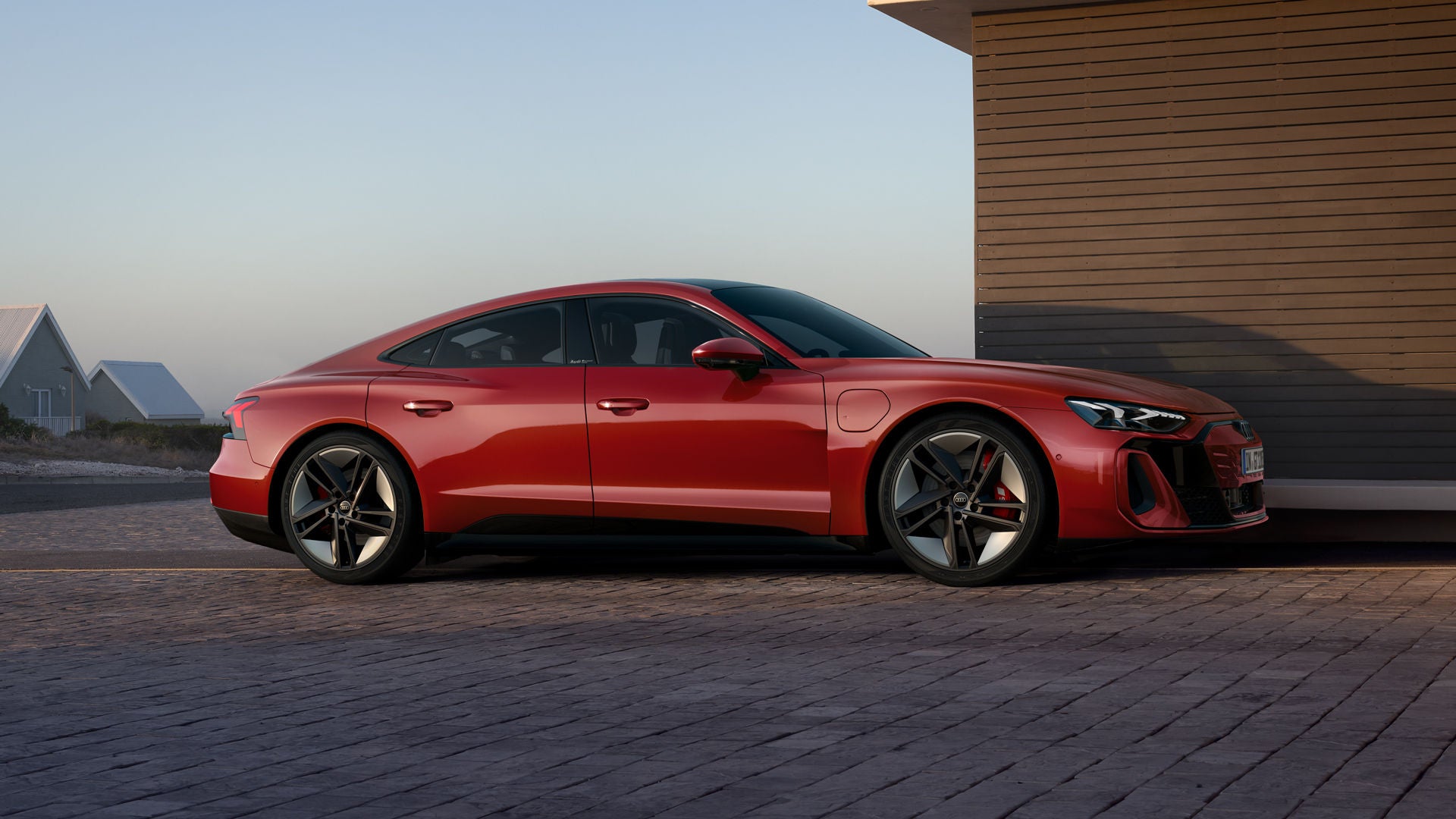 Ein roter Audi S e-tron GT parkt neben einem Haus, eine minimalistische Architektur und ruhige Landschaft im Hintergrund.