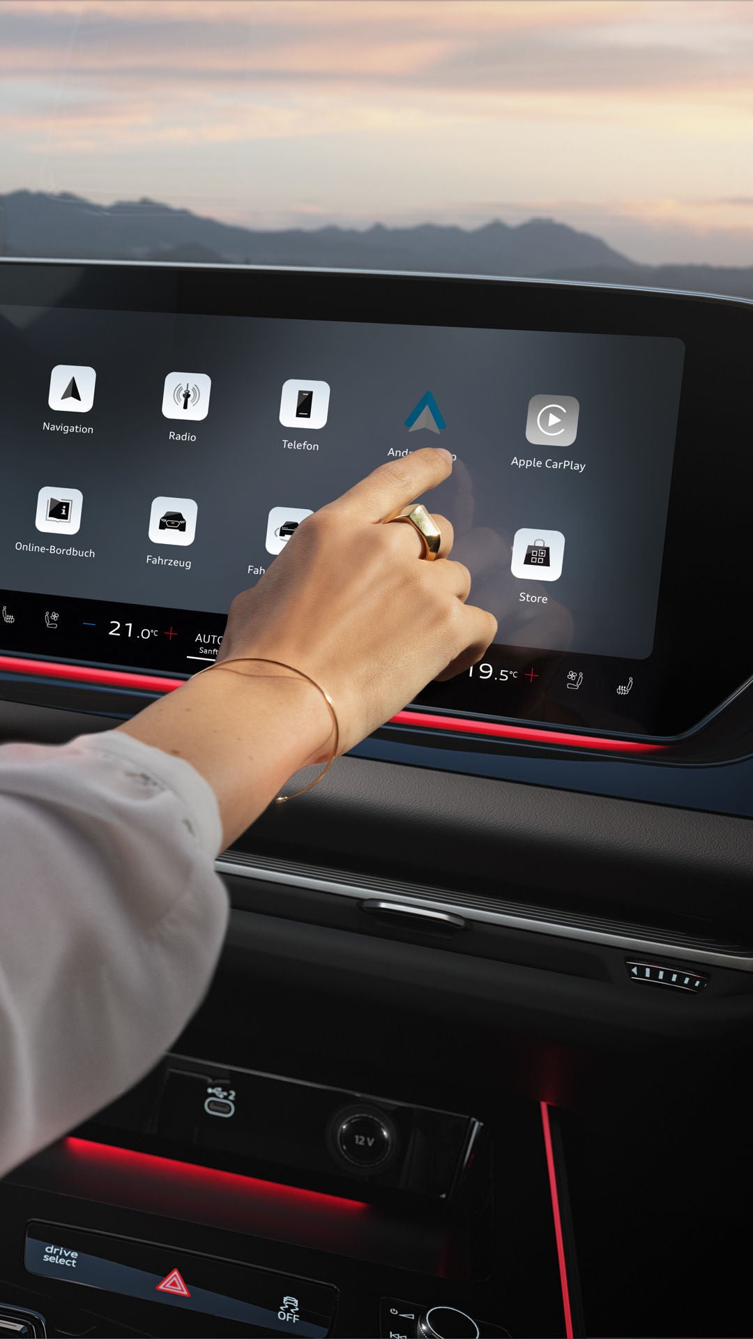 Primo piano del cockpit di un’Audi. Il braccio destro di una donna entra nell’inquadratura da sinistra e tocca l’ampio display digitale centrale.