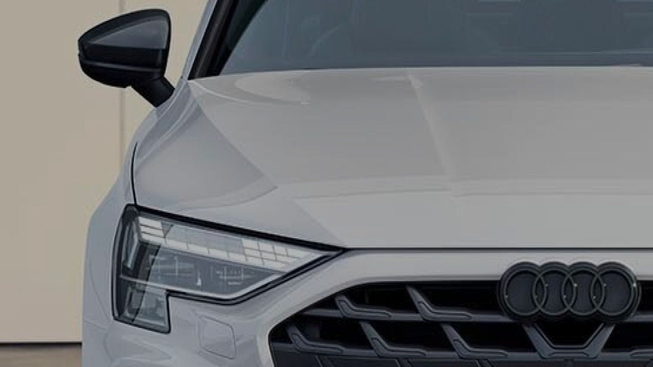 Close up of the front of a white Audi, with Audi logo visible and lights