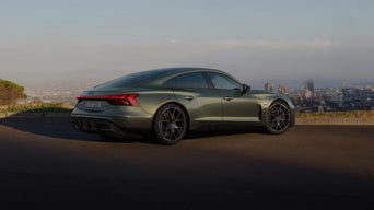 A grey Audi RS e-tron GT parked in front of a modern stone house, showcasing its sporty design and bold front grille.