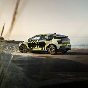 A side view of the Audi A2 e-tron with yellowish vinyl wrap against a picturesque beach backdrop.