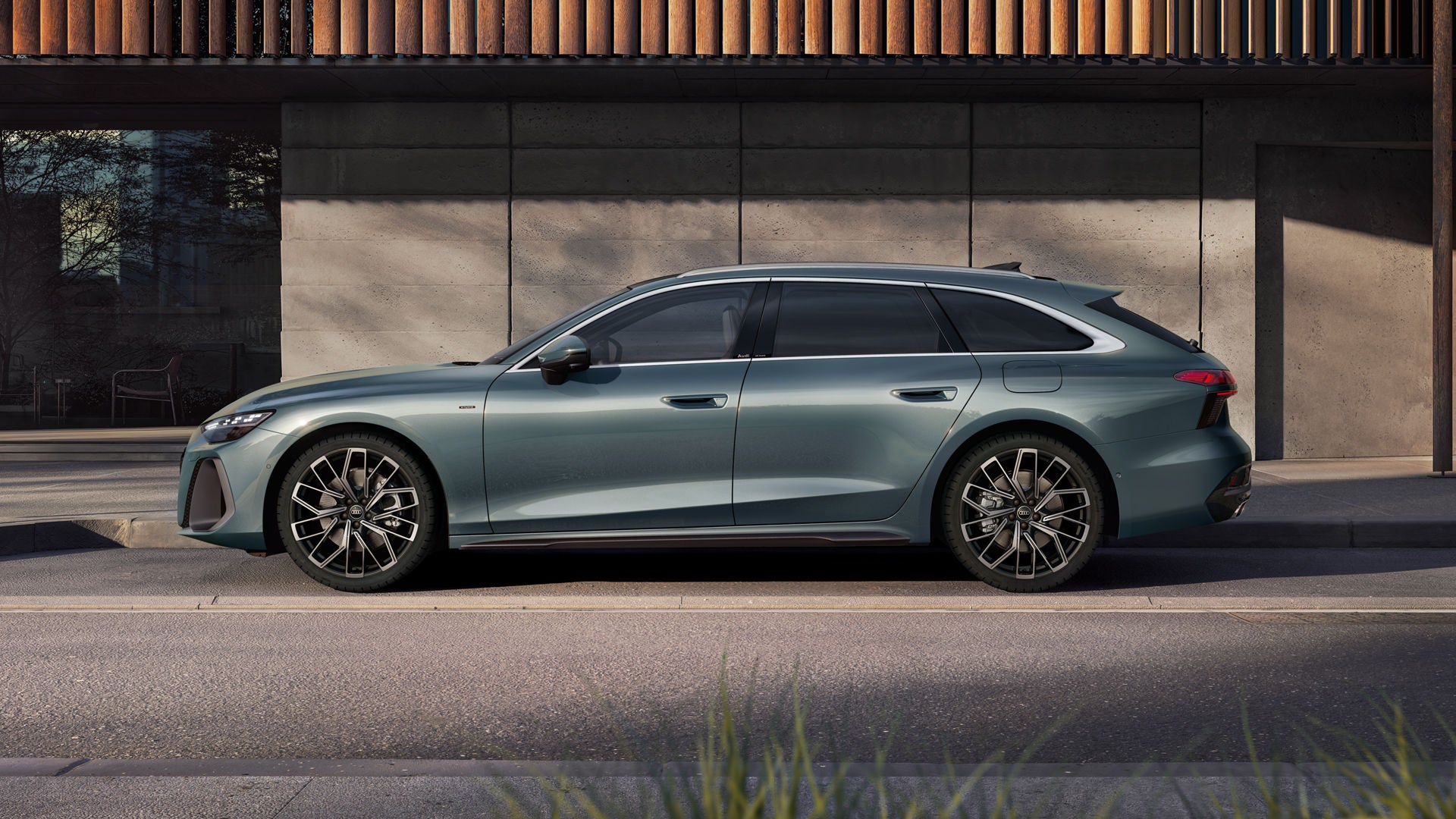 Der A6 Avant e-hybrid in Morgentaugrün steht im Seitenprofil vor der Fassade eines Gebäudes.