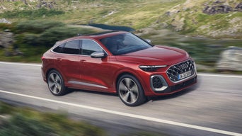 Roter Audi SQ5 Sportback fährt bei Tageslicht auf einer kurvigen Landstraße durch grüne Hügellandschaft.