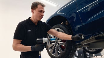 Mechaniker in schwarzer Audi-Uniform zieht Radbolzen an blauem Fahrzeug fest.