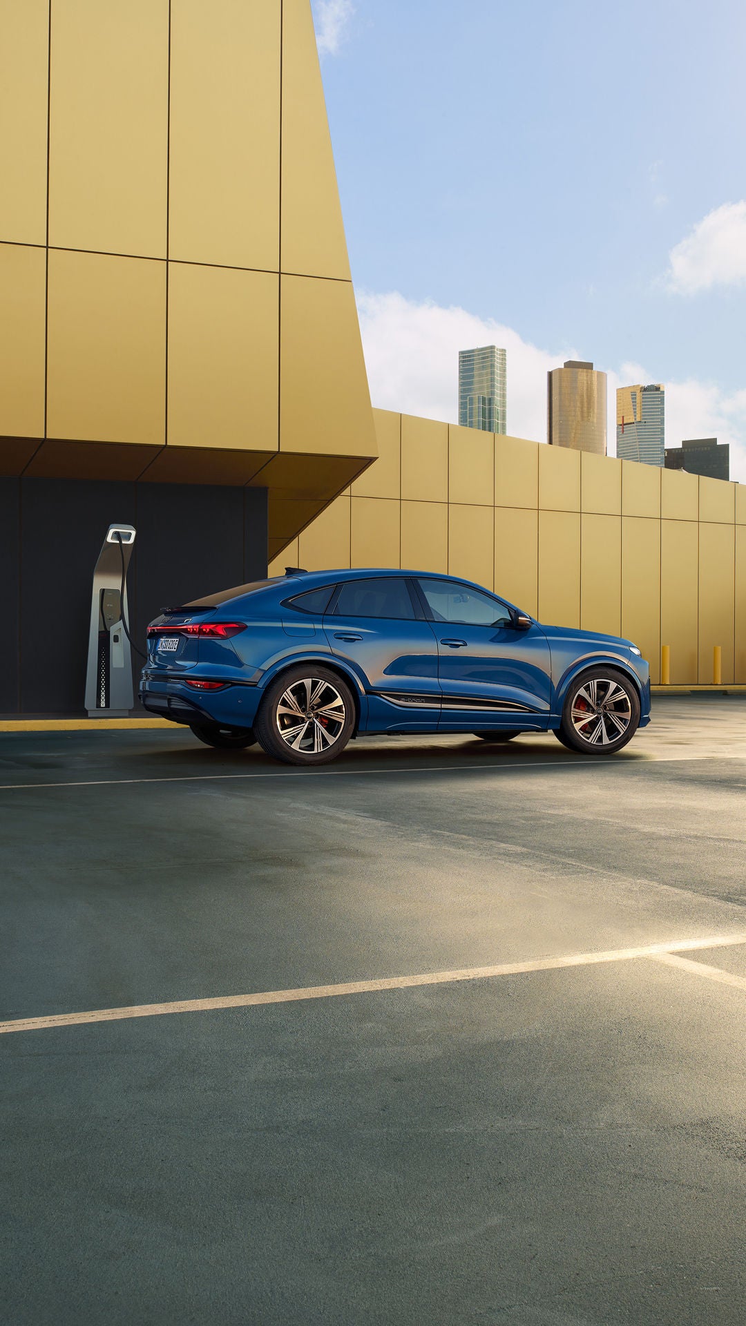 A blue SQ6 Sportback e-tron parked in front of an EV charger at the base of a yellow building