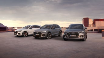 Drei Audi-SUVs nebeneinander auf einem Parkdeck bei Sonnenuntergang, im Hintergrund moderne Gebäude.