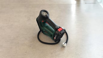 Akku-Druckluftpumpe mit integriertem Manometer und Luftschlauch auf heller Oberfläche.