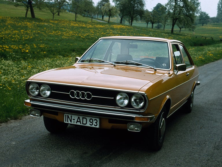 Frontansicht eines Audi 80 GL in orange vor einer Blumenwiese