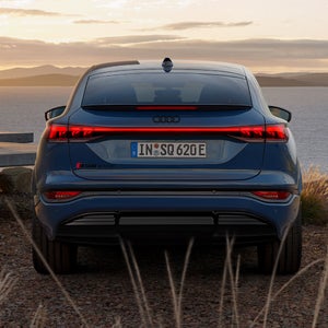 Heckprofil des SQ6 Sportback e-tron, auf Schotter parkend. Im Hintergrund das Meer bei Sonnenuntergang.
