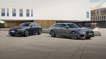 Zwei graue Audi Avant stehen versetzt auf einer weitläufigen Steinplaza vor einem großen, weißen Kubusgebäude.