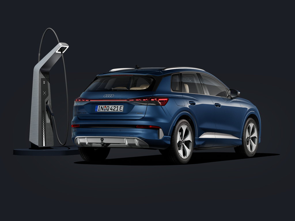 Der Q4 SUV e-tron von schräg hinten auf dunklem Hintergrund, flankiert von einer modernen Ladesäule.