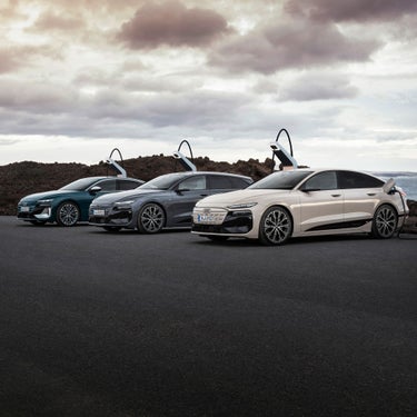 An Audi A6 Sportback e-tron performance, Audi A6 Avant e-tron performance and an Audi S6 Sportback e-tron are parked at charging points in front of the sea