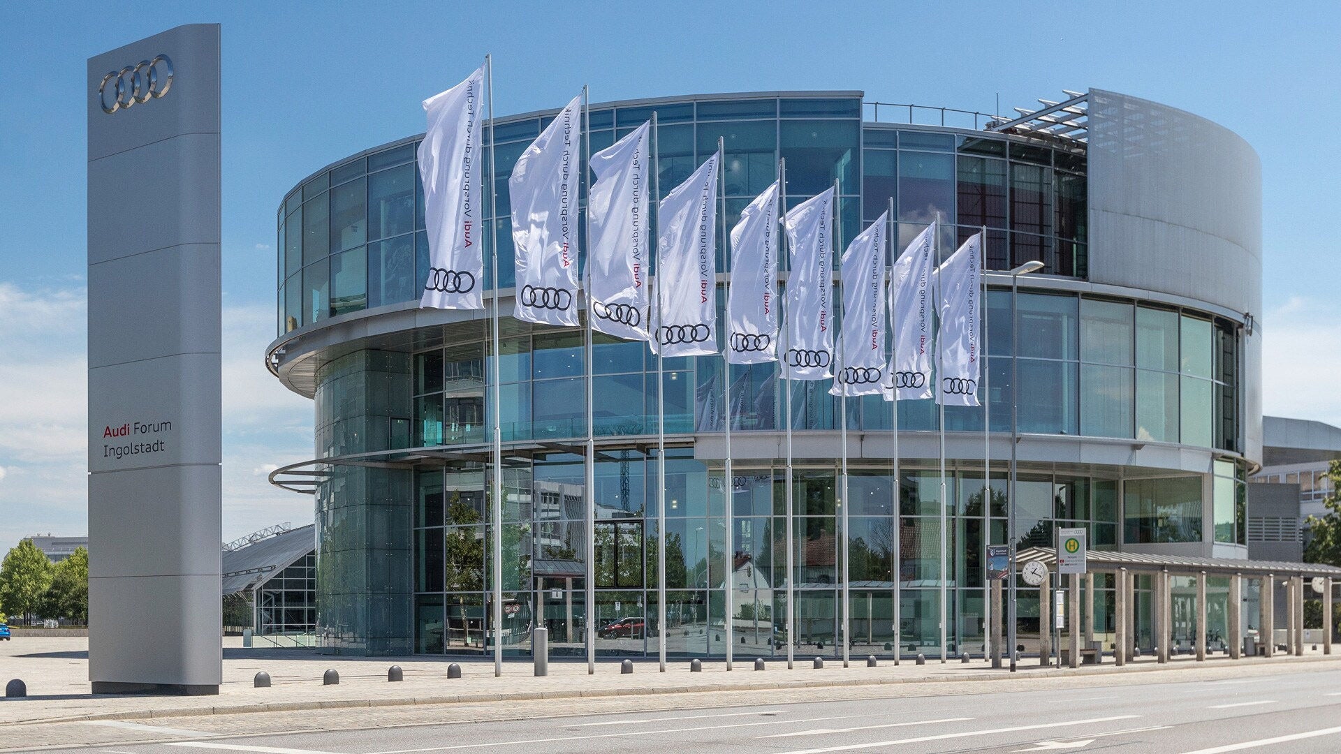 Audi Forum Ingolstadt mit Glasfassade und vielen weißen Audi-Flaggen.