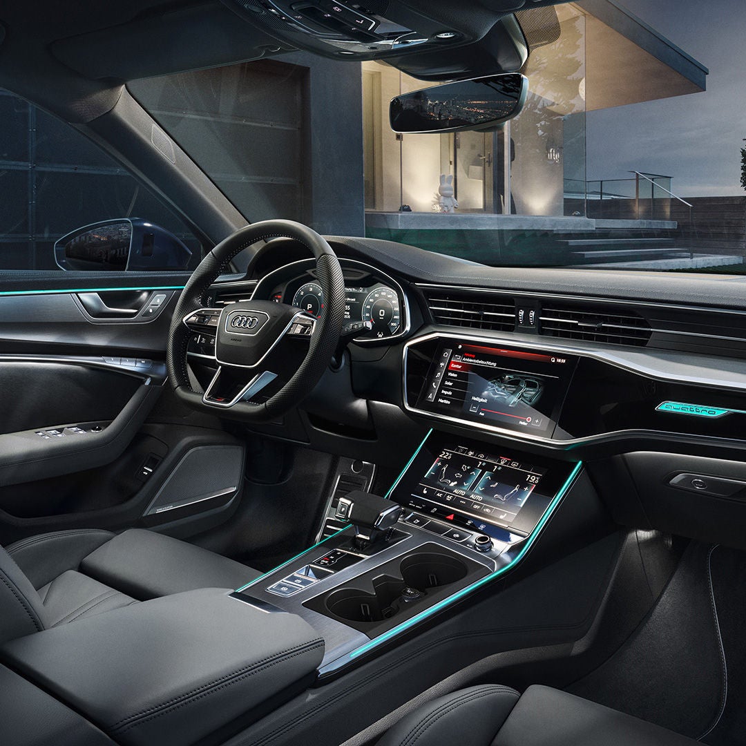 En kvinna sittandes i en soffa i en Audiverkstad och tittar i en tidning, bakom står en man och en pojke vid en blå bil