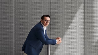 Giorgio Delucchi in blauem Sakko lehnt an einem Geländer vor einer perforierten Metallwand und blickt zur Kamera.