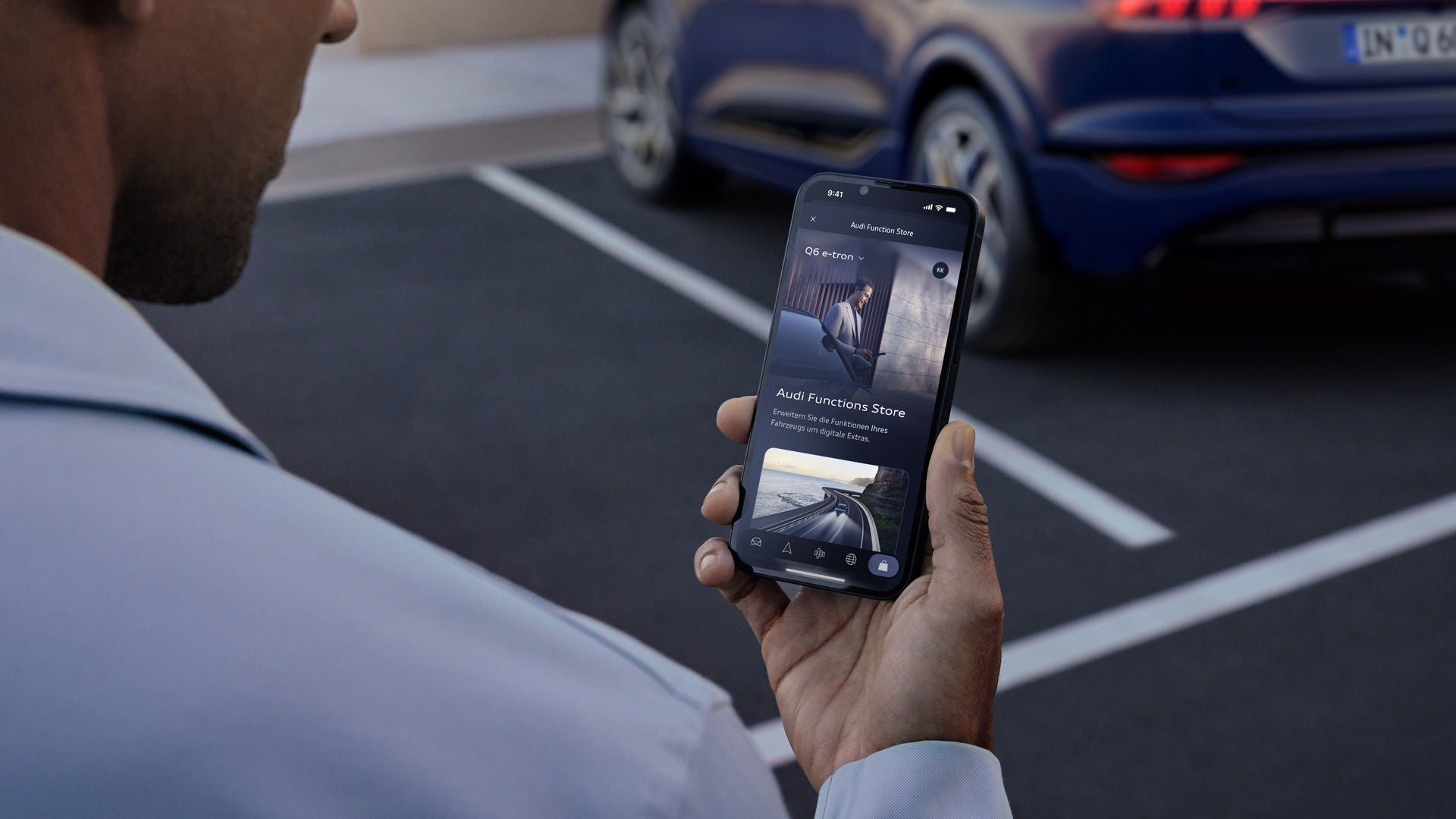 Ein Mann in grauem Anzug steht vor einem Haus und schaut lächelnd auf sein Smartphone neben einem geparkten Audi.