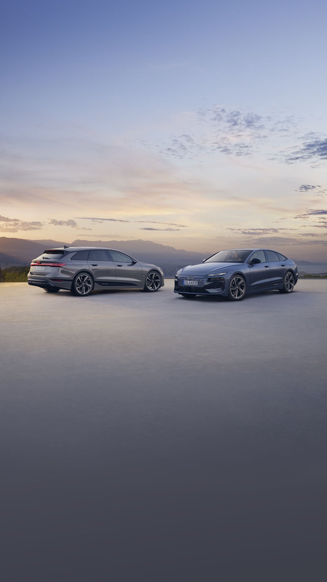 Two sleek, modern cars parked on a flat surface during sunset. The sky is colourful with clouds, creating a serene and elegant atmosphere.