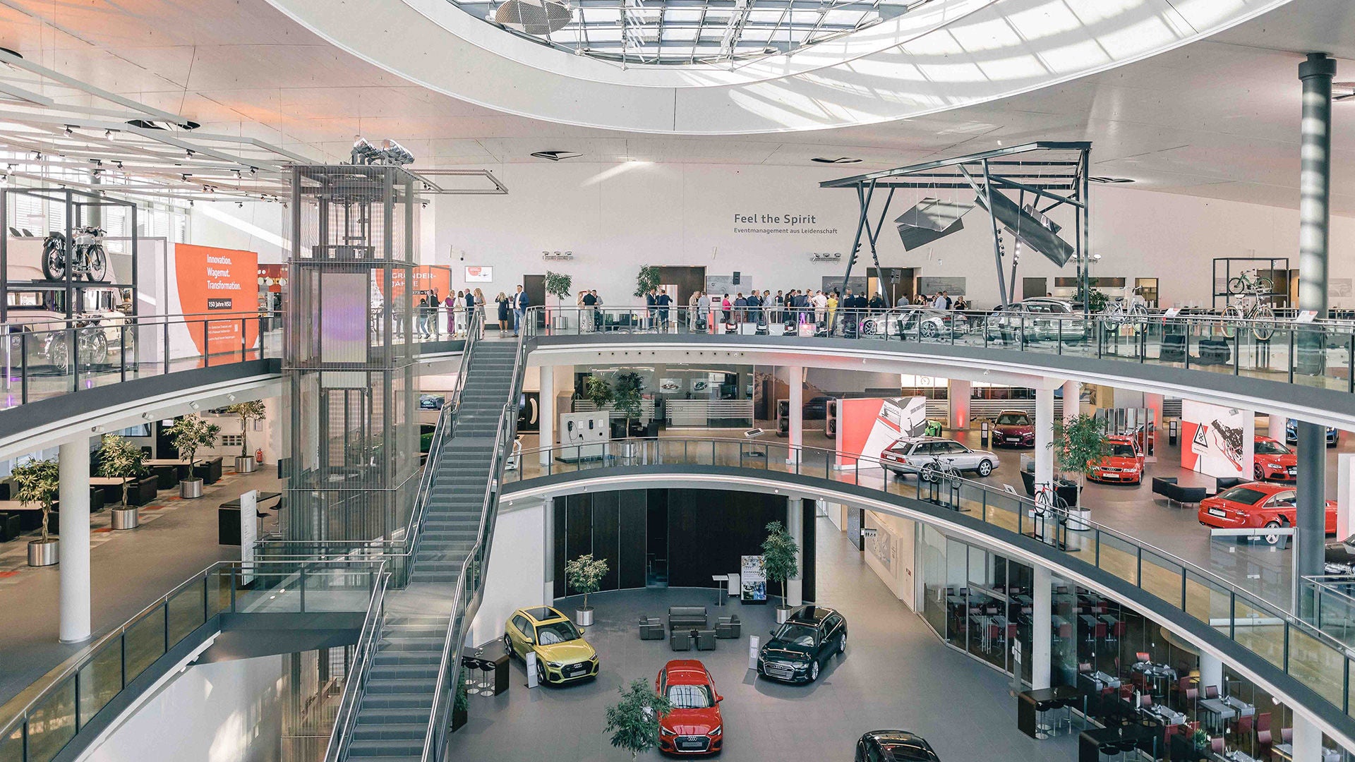 Helle, mehrstöckige Autoausstellung mit Rolltreppe, Glasdach und mehreren ausgestellten Fahrzeugen.