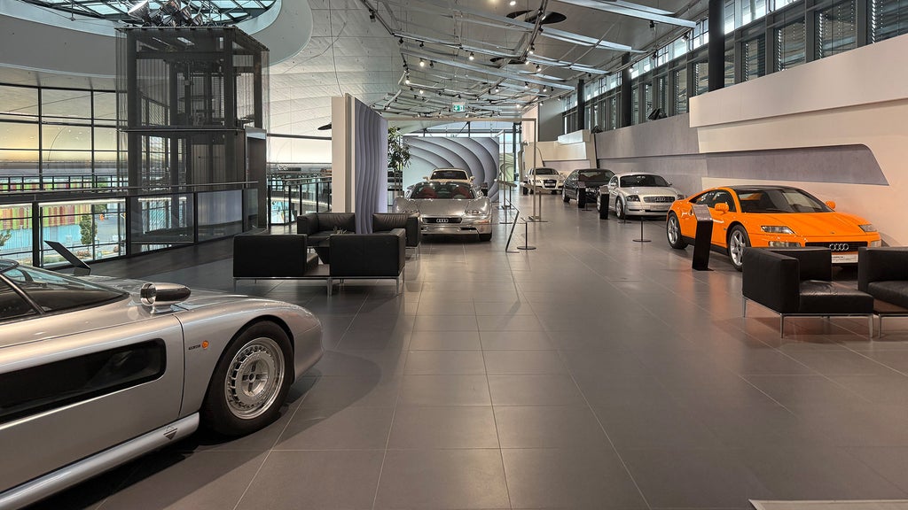 Weitläufige Audi-Ausstellungshalle mit mehreren Fahrzeugen, darunter ein auffälliger orangefarbener Sportwagen.
