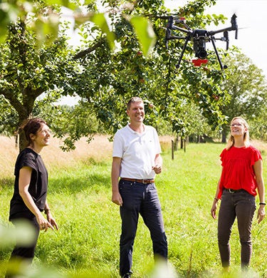 Three people watch a drone fly